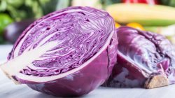 A red cabbage sliced in half in front of vegetables